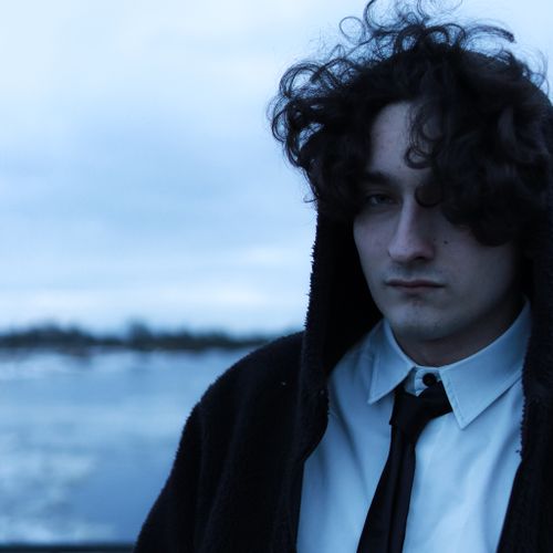 Free Portrait of a young man with curly hair in formal attire, standing outdoors in muted evening light. Stock Photo