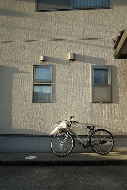 Free Bicycle parked against a sunlit building wall, casting shadow on asphalt. Stock Photo