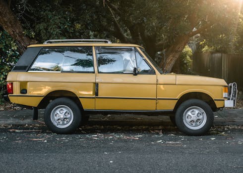 Side view of a classic yellow SUV parked on a tree-lined urban street during the day.