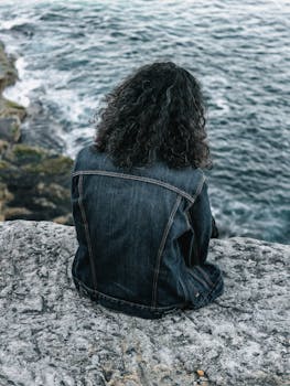 阴天，一名女子坐在悬崖边，从后视镜中俯瞰广阔的海景