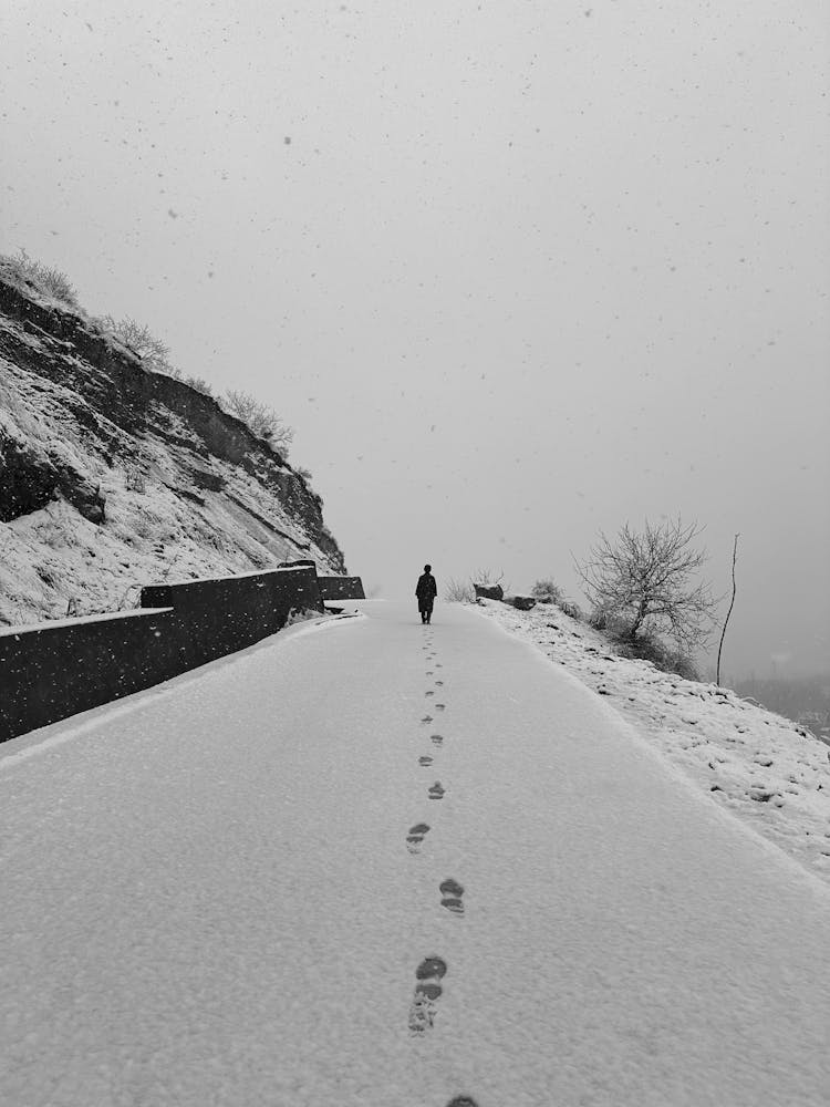 Black And White Photograph Of A Person Walking On A Mound, And Leaving Footprints On Snow