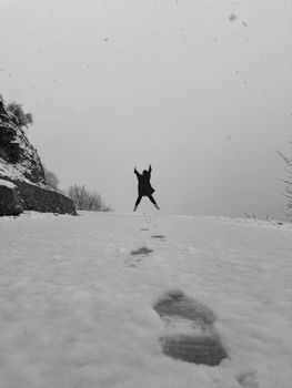A person jumps playfully on a snowy path during a snowstorm, creating a dynamic winter scene.