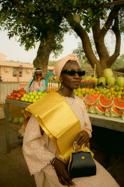 A woman in a yellow dress and gold purse sitting on a bench