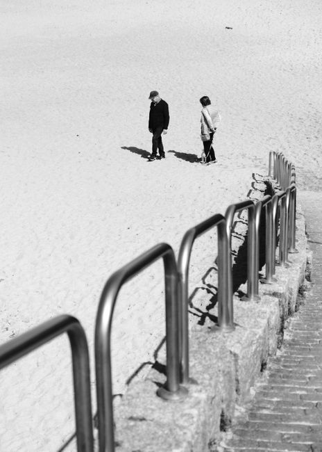 Black and white photo of an elderly couple walking on the beach in A Coruña, Spain.