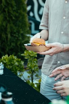 Close-up of hands holding a burger in an outdoor setting. Casual and relaxed atmosphere.
