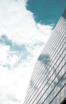 一座高大的现代玻璃建筑映衬着明亮的天空，窗户上反射着云层