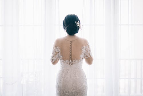 흰색 커튼 근처 흰색 레이스 웨딩 드레스를 입고 여자