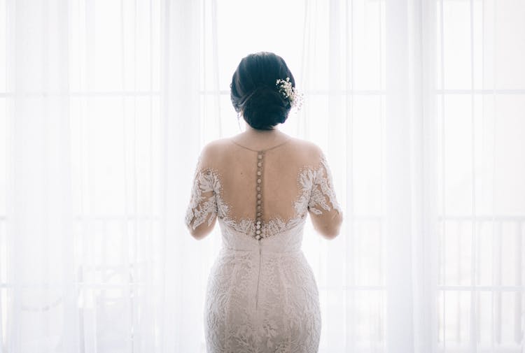 Woman Wearing White Lace Wedding Dress Near White Curtain