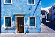 在明亮的日光下，一座带有木窗的古老蓝色乡村建筑矗立在空荡荡的街道上