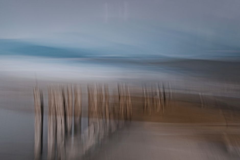 Dreamlike coastal scene with blurred wooden posts and serene water.