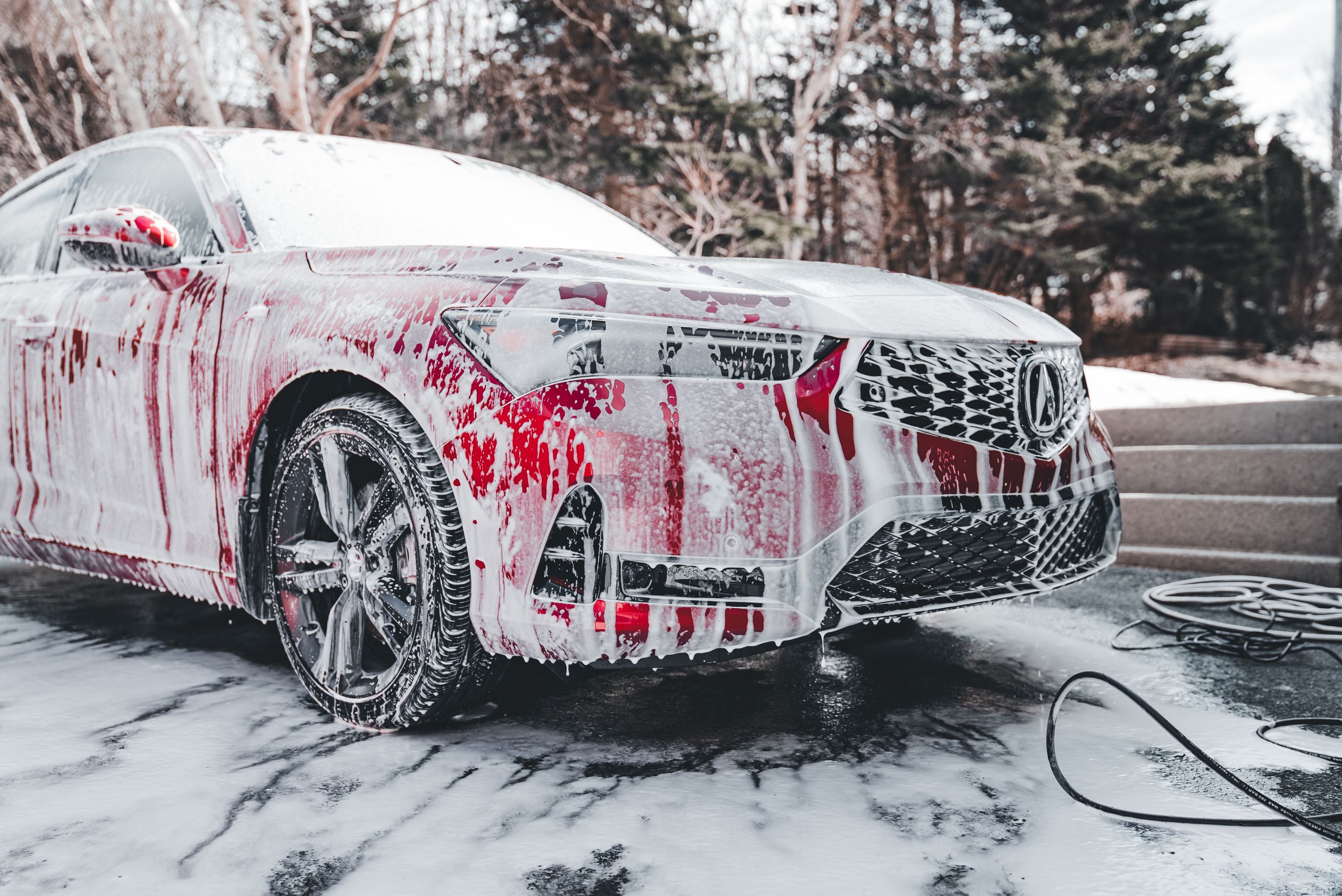 Red sports car covered in thick white foam from a foam cannon during a two-bucket wash