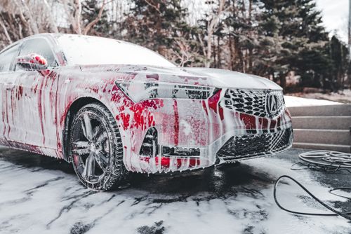 Free A vibrant red car covered in soapy foam during a thorough outdoor wash under daylight. Stock Photo