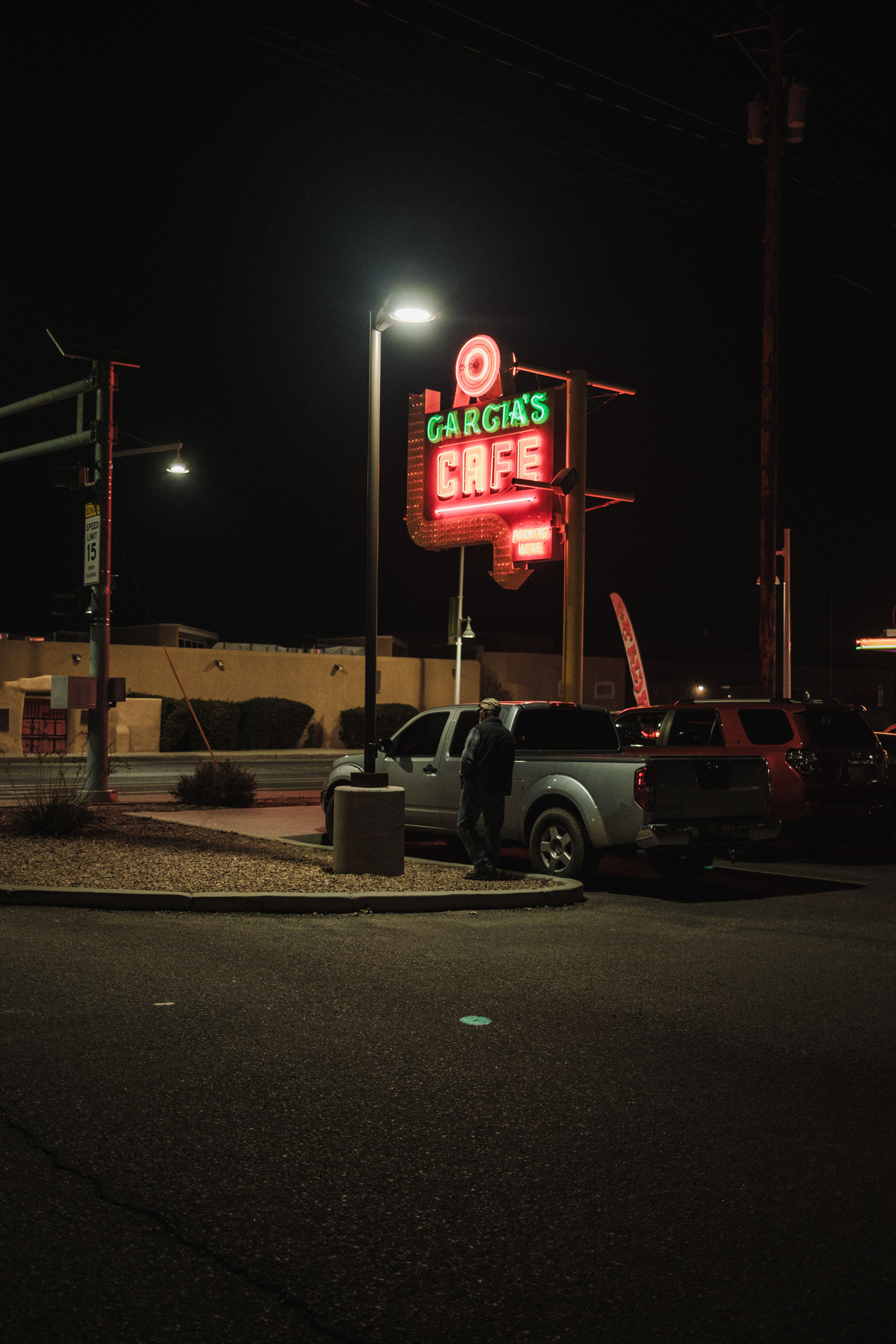 A neon café sign glows in a dimly lit parking lot at night, capturing urban nightlife.