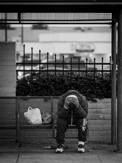 Free A man in distress sits at a bus stop with bags on a bench in an urban setting. Stock Photo