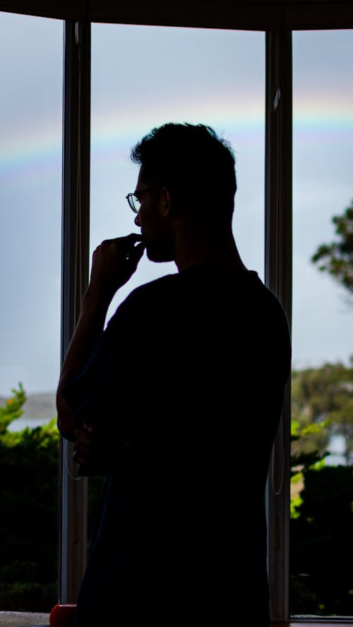 A man is looking out the window at a rainbow