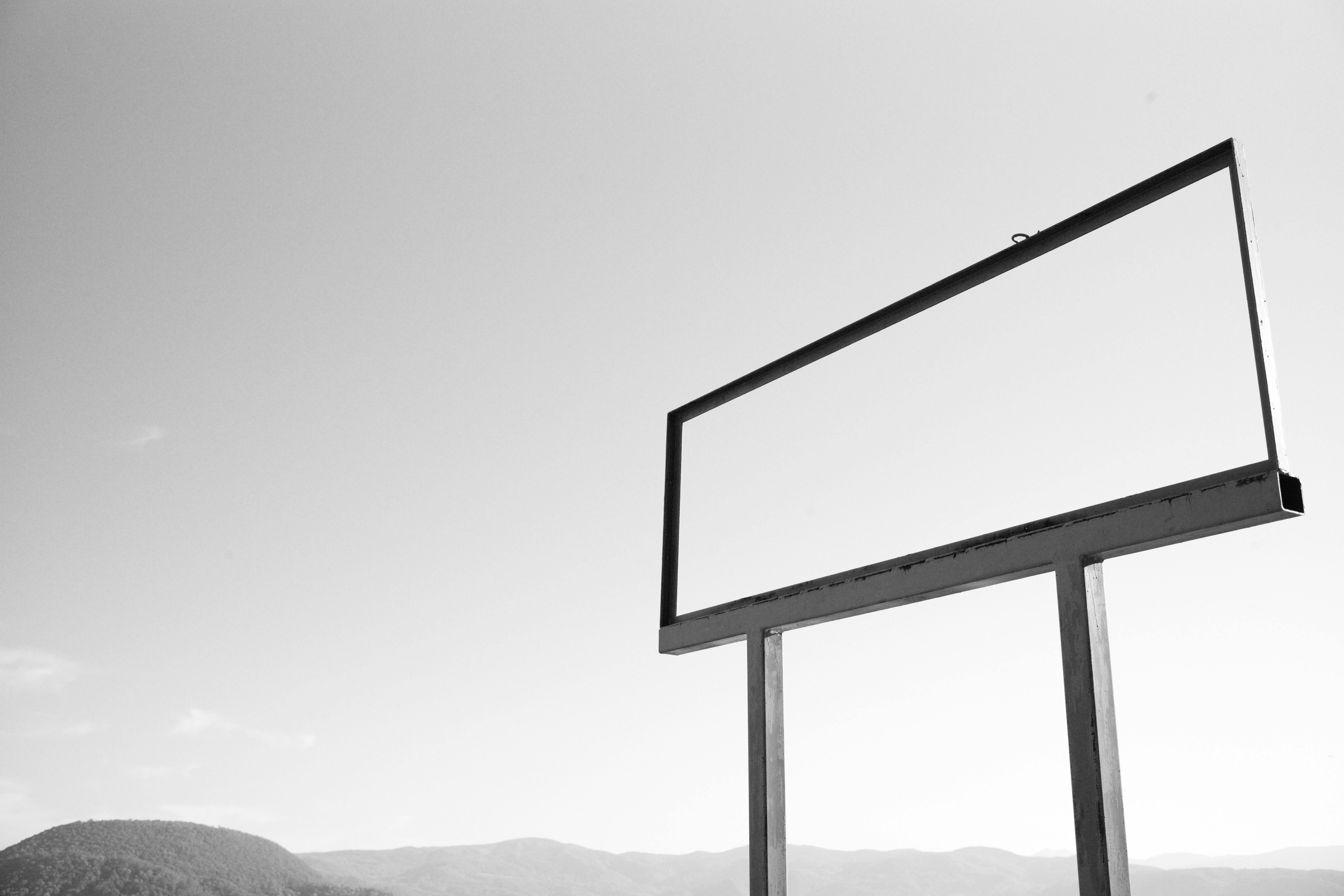 A solitary, empty billboard stands in a rural landscape under a clear sky.