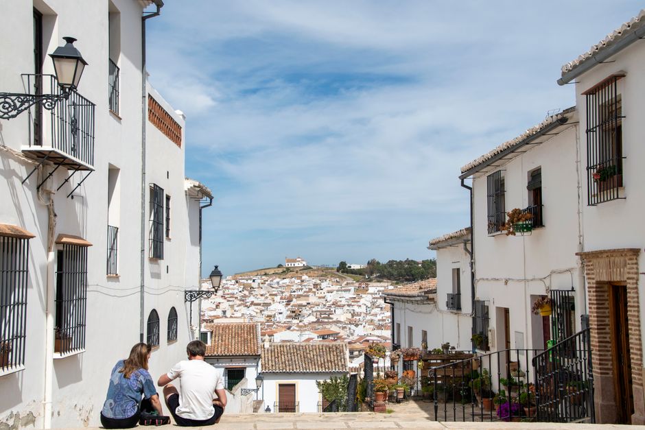 A couple sits in an alley enjoying a scenic view of a white Spanish town's architecture.