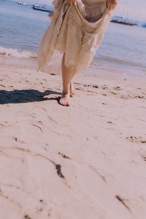 Photo of a Woman in a Dress Walking Barefoot on a Beach 
