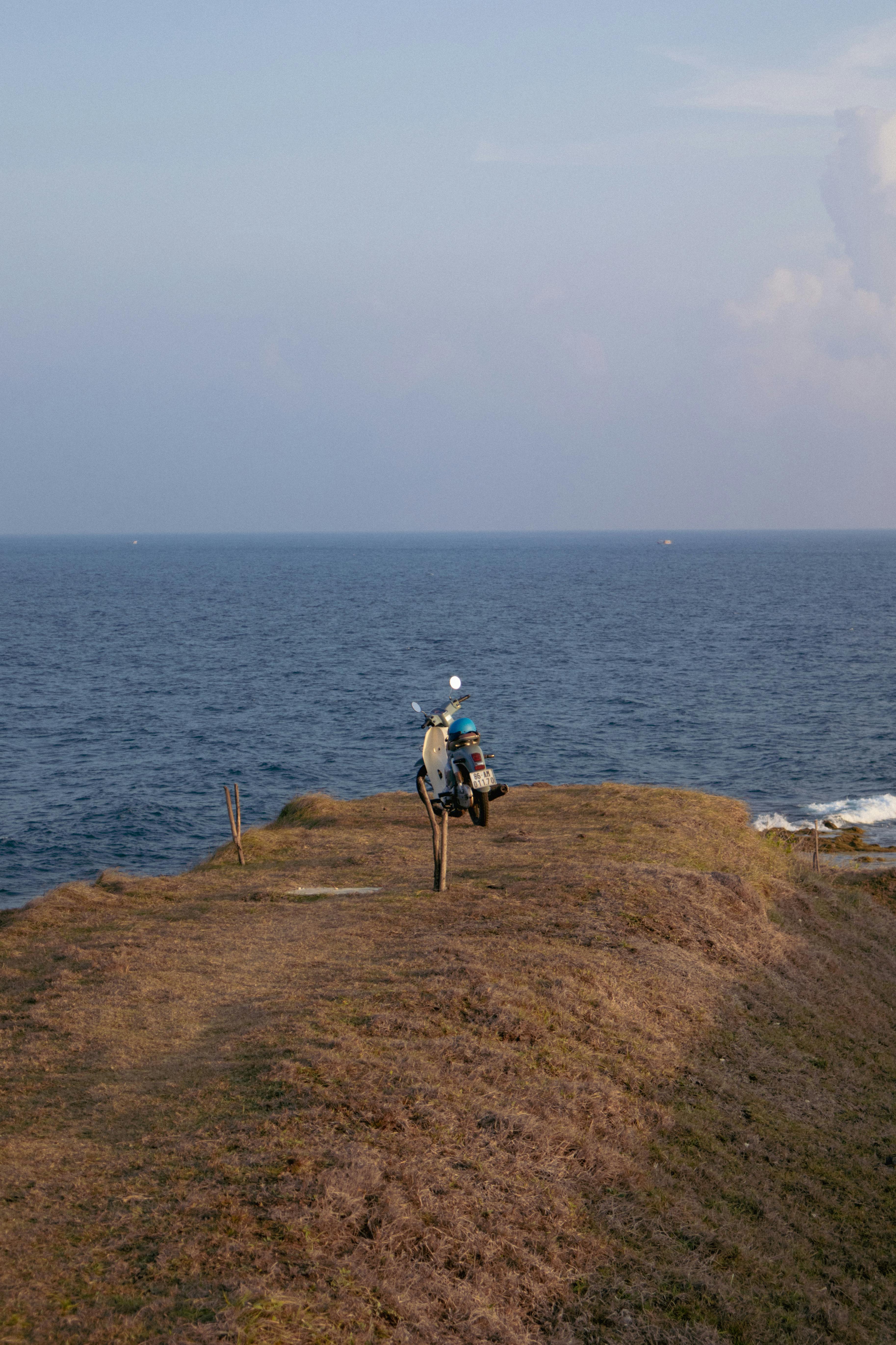Motorbike parked on a grass-covered cliff by the sea, offering a serene coastal view at dusk.
