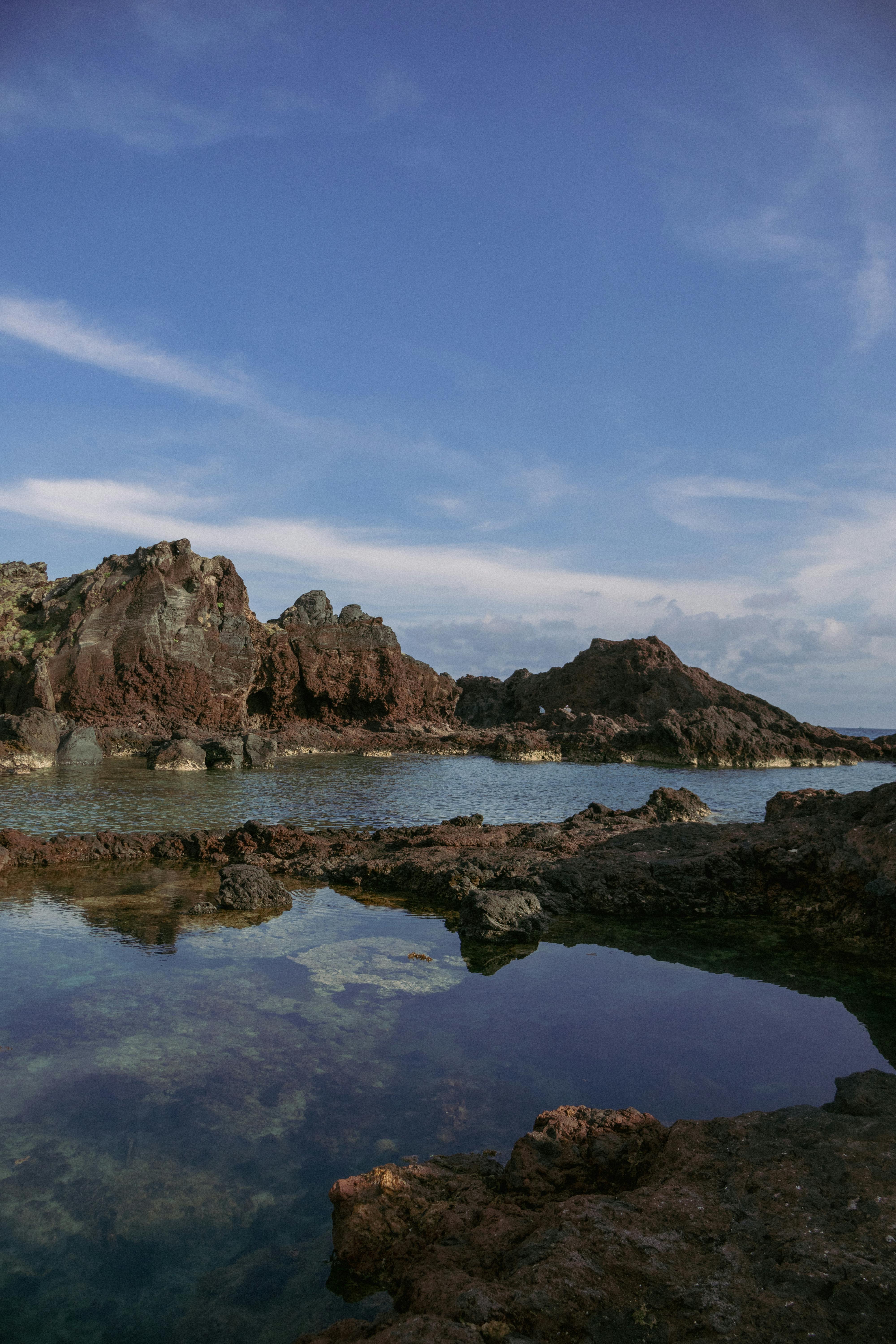 Explore a tranquil rocky coastline with stunning water reflections under a clear blue sky.
