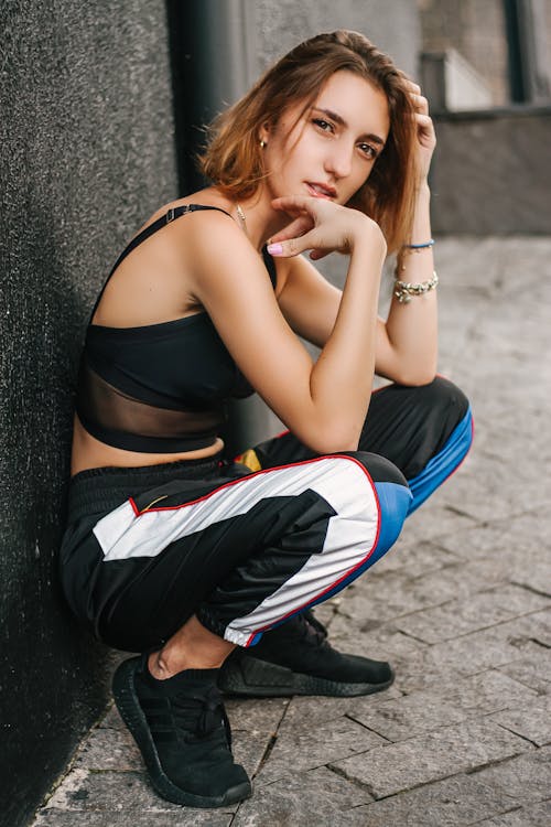 Free Smiling Woman Wearing Black Bra Sitting Against the Wall and Looking Side Stock Photo