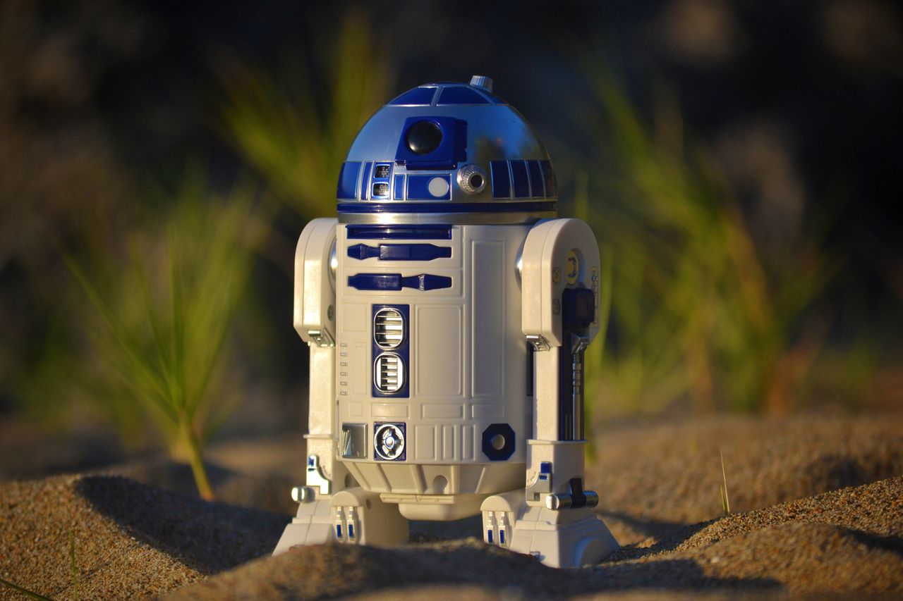 close up of an r2 d2 toy standing on sand set against a green backgrou