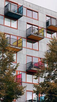 Vertical view of a modern residential block with colorful balconies and trees.