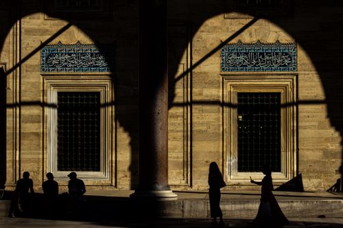Free Silhouetted figures stand against the warm tones of a mosque's exterior at sunset, creating dramatic shadows. Stock Photo