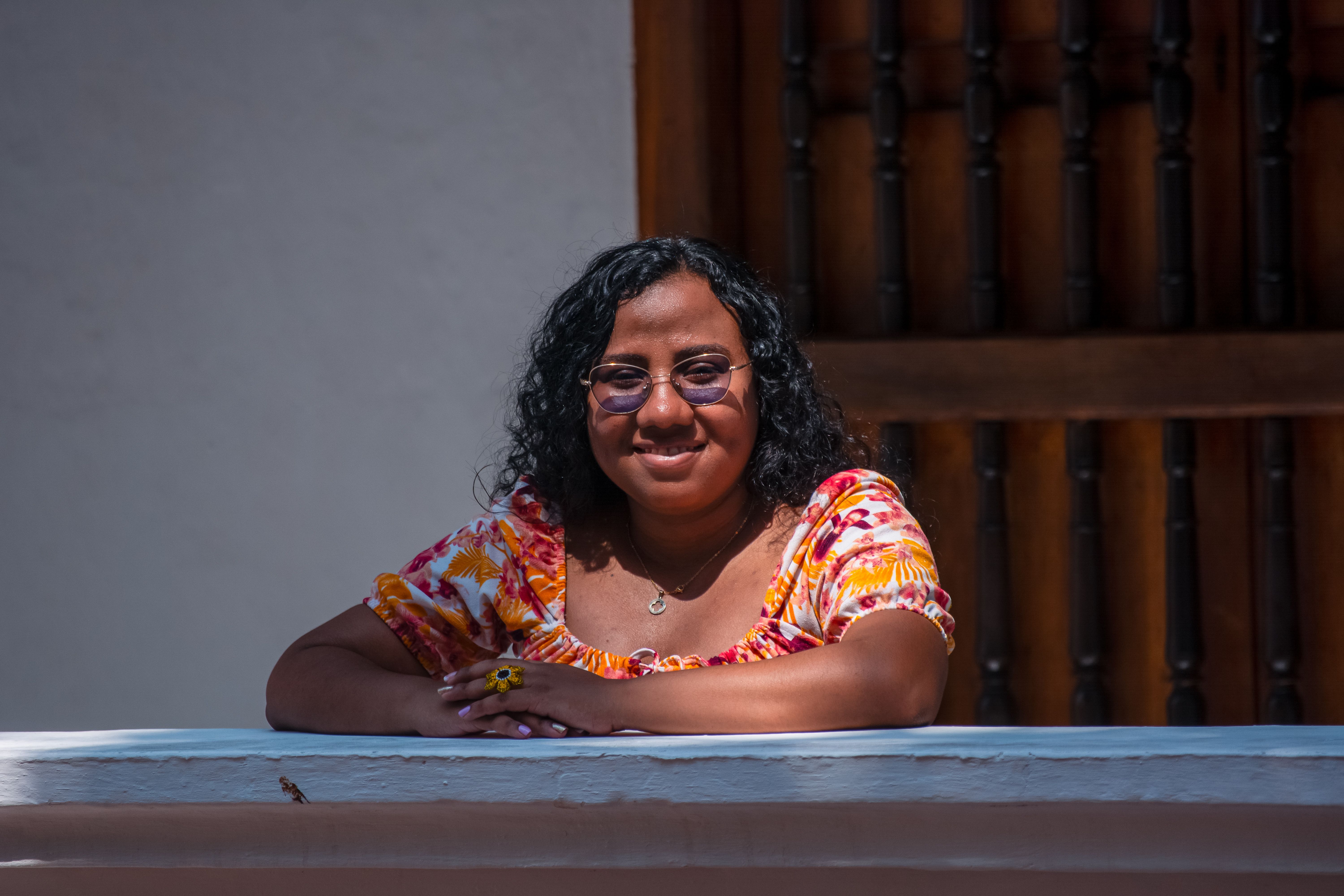 Joyful woman in floral top enjoying a sunny day on the balcony.
