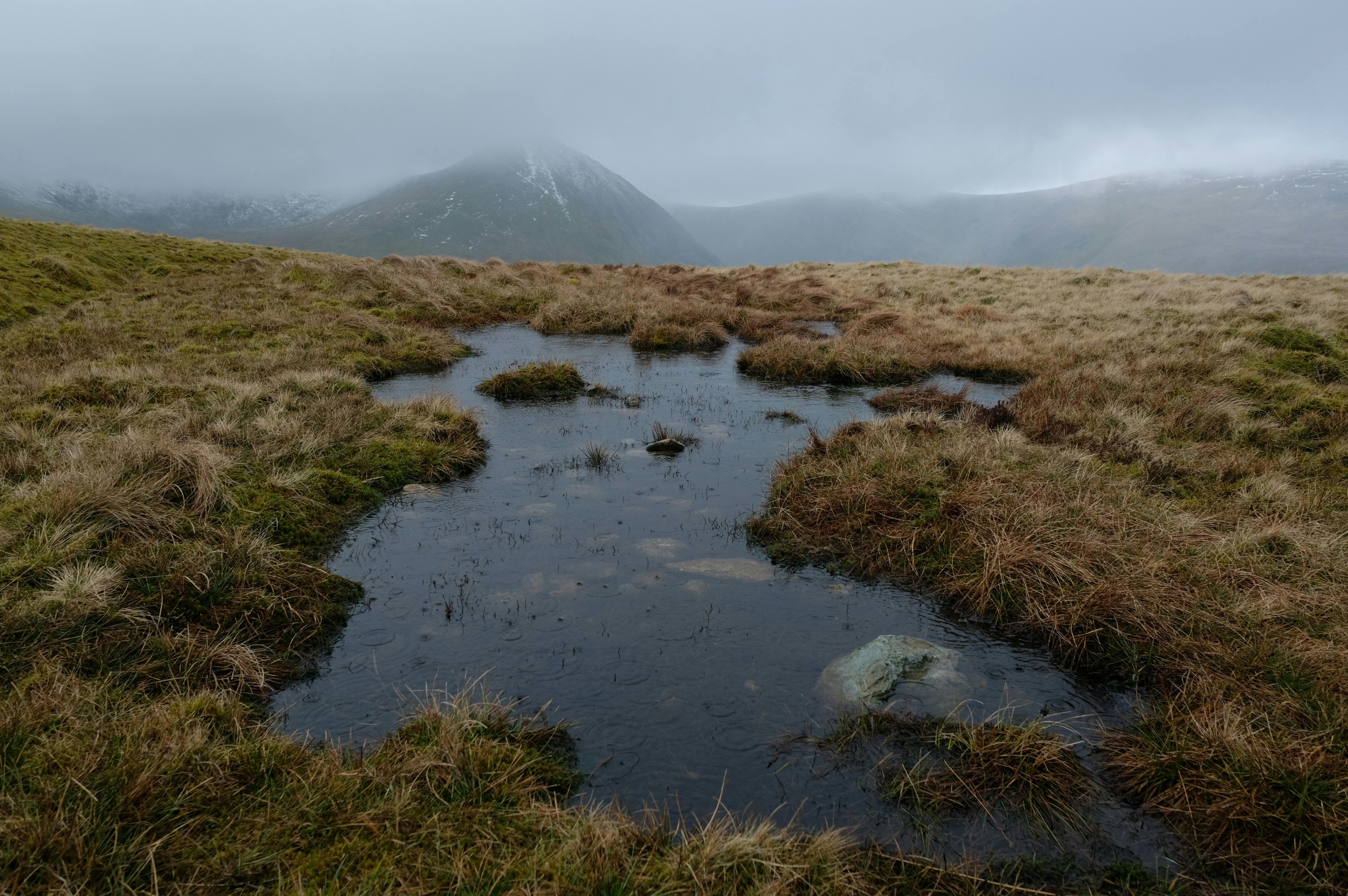 Depicts a serene foggy pond with mountain view in Glenridding, England. Perfect for atmospheric landscape imagery.