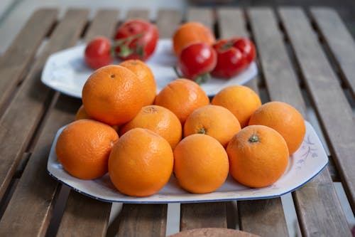 A plate of oranges and tomatoes on a wooden table