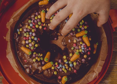 A person's hand is touching a chocolate cake with carrots and sprinkles