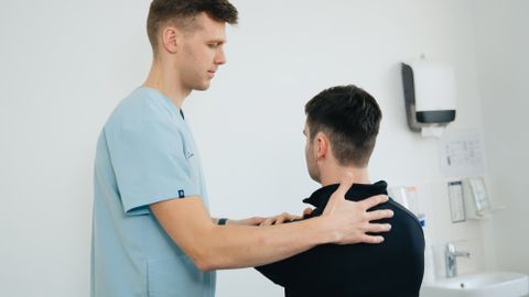 Physiotherapist working with a patient in a clinical setting, focusing on shoulder therapy.