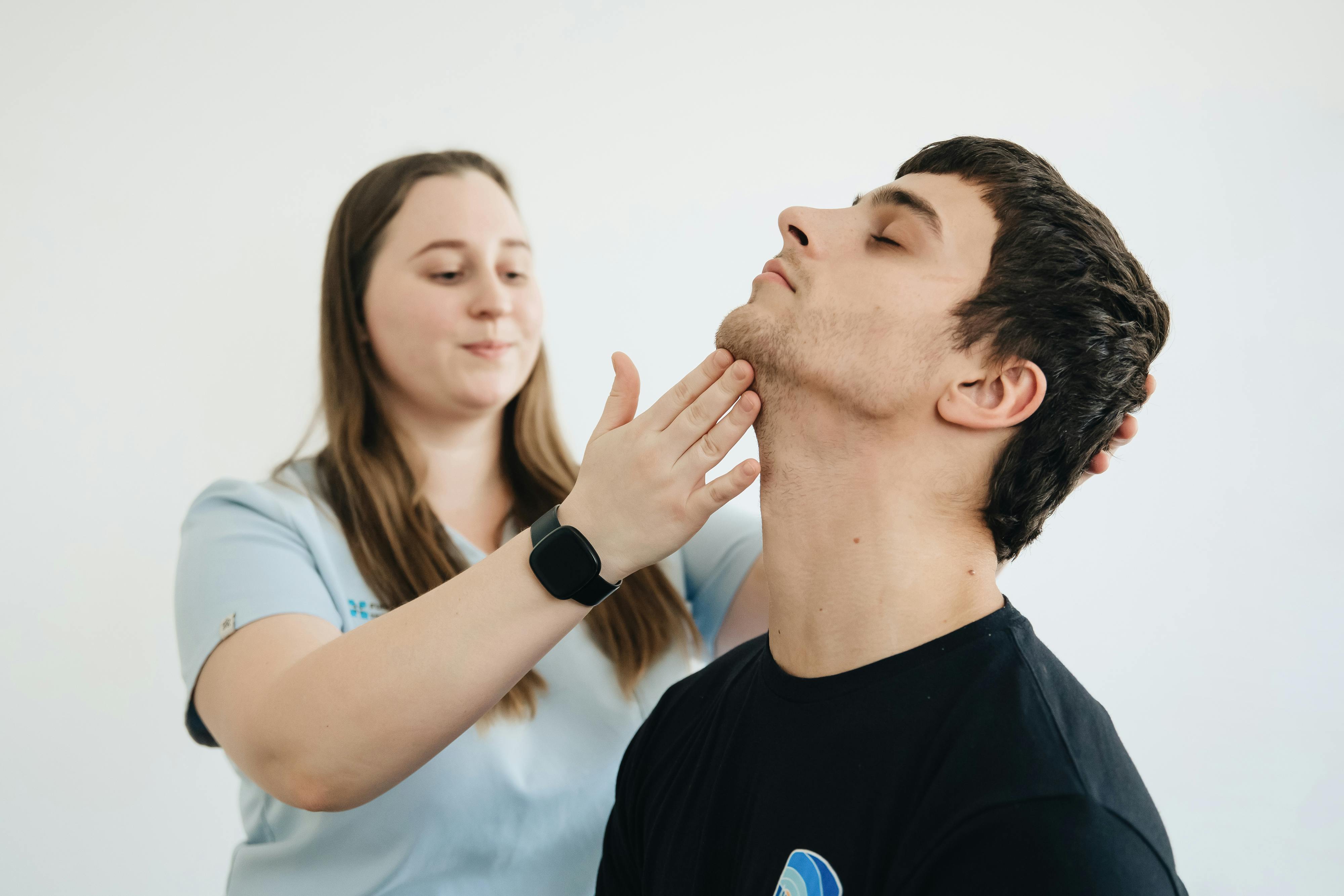 A physiotherapist performs therapy on a male patient's neck in a clinic.