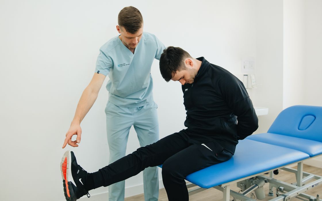 Physiotherapist guiding a patient through a leg-stretching exercise on a treatment table