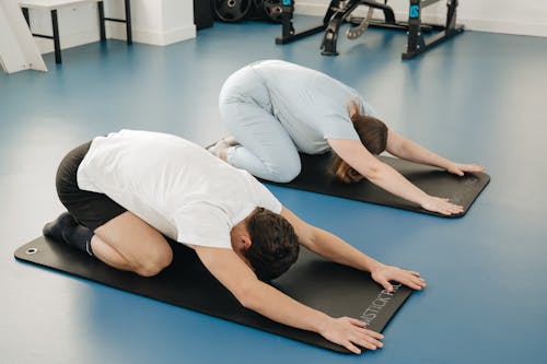 Two people doing yoga on a mat in a gym
