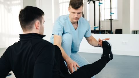 A physiotherapist assisting a patient in leg exercises during a rehabilitation session in a clinic setting.