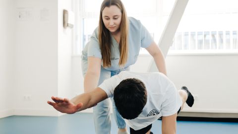 A physiotherapist assists a patient in stretching exercises indoors.