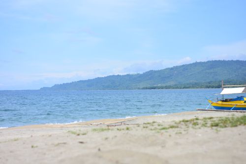 Free Peaceful beach scene with a colorful fishing boat and lush green hills in the background. Stock Photo