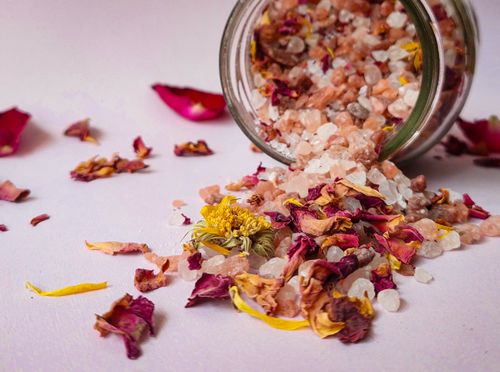 Free Pink Himalayan salt and dried flowers spilling from a glass jar on a light surface. Stock Photo