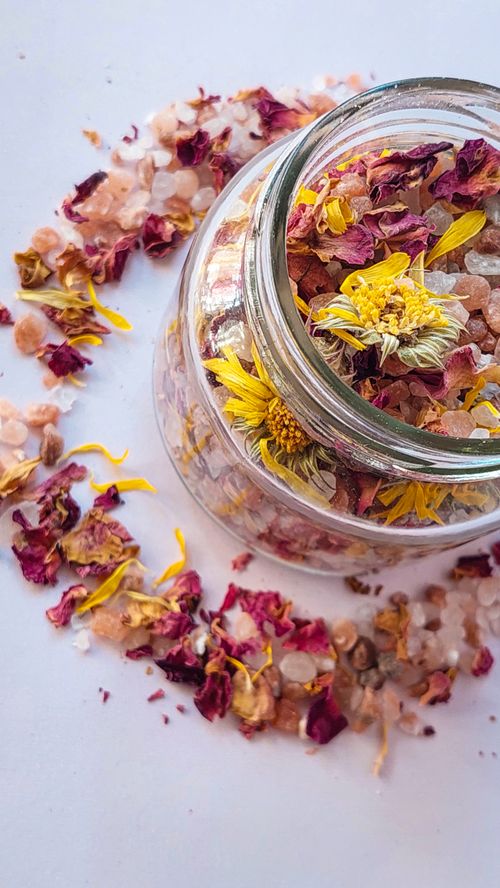 Free Close-up of a glass jar with dried petals and herbs, surrounded by pink Himalayan salt on a white background. Stock Photo