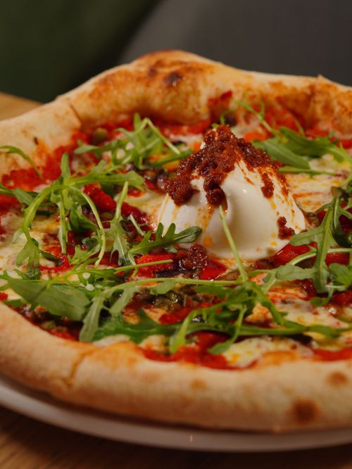 Free Close-up of a gourmet pizza topped with fresh arugula, creamy burrata, and a spicy tomato sauce. Stock Photo