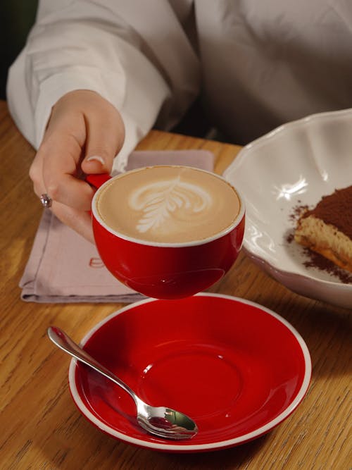 A person is holding a cup of coffee and a plate of cake