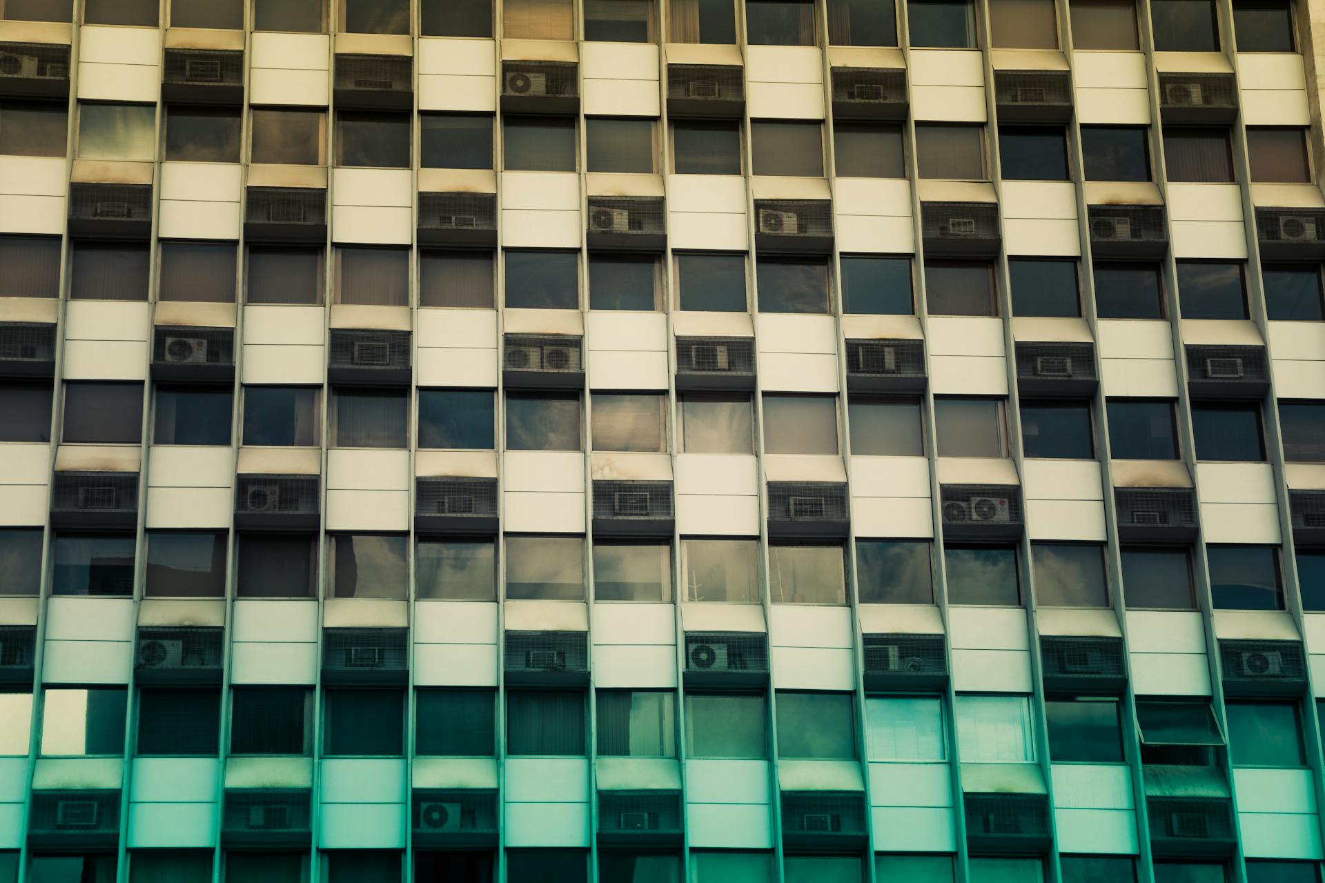 Contemporary office building featuring a grid of glass windows and air conditioners.