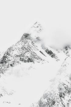 A dramatic snow-covered mountain peak partially shrouded in mist, capturing the beauty of winter.