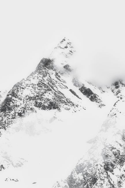 A dramatic snow-covered mountain peak partially shrouded in mist, capturing the beauty of winter.