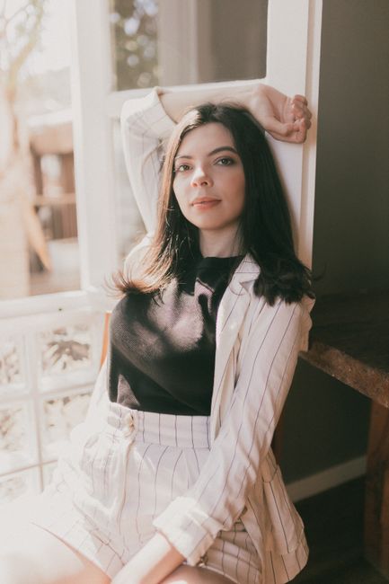 Stylish woman in striped outfit poses by a sunlit window, exuding elegance and confidence.