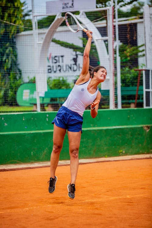 A woman in blue shorts and white tank top is playing tennis