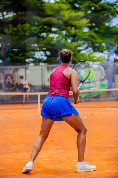 A woman in blue shorts and red shirt playing tennis