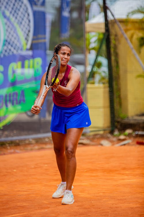 A woman in blue shorts and a red shirt is playing tennis